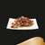 Chunks of meat in gravy on a white square plate, garnished with two green chive stalks, shown against a black background.