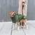 Chien portant un manteau vert avec col montant et bandes réfléchissantes, tenu en laisse par une personne en manteau beige. Badge rond visible sur le manteau du chien.