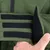 Gros plan sur une fermeture à scratch noire sur un manteau vert, tenue par une main. Matière extérieure lisse, intérieur en tissu doux visible.