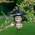 Black metal bird feeder with spiral design, filled with two fat balls, hanging from a tree branch in the garden.