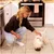 Kvinna matar en liten vit hund som äter ur en matskål. Scenen visar en utfodringssituation i ett kök. Kvinna matar en liten vit hund som äter ur en matskål. Scenen visar en utfodringssituation i ett kök.