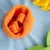 Orange fleece-legetøj i blomsterform på lyseblå baggrund, egnet til interaktiv leg eller aktivering.