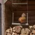 Huhn sitzt auf einer Hühnerwippe aus Metall, aufgehängt mit Seilen in einem Holzschuppen über gestapeltem Brennholz.