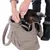 Petit chien noir et feu dans un sac de transport en tissu bouclé beige, une personne attache le collier du chien à l’intérieur du sac. Marque Zolux visible sur le collier.