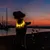 Chien portant un collier lumineux jaune allumé, visible en extérieur au crépuscule près d’un plan d’eau et de voiliers.