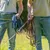 Deux personnes en jeans tenant plusieurs laisses pour chien, une bleue et une rouge, à l’extérieur. Sac banane visible sur l’une des personnes.