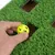 Hand places yellow plastic ball into a hole of a green play mat with artificial grass.