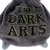 Texte brodé sur tissu gris : THE DARK ARTS (en anglais).