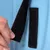 Primer plano de cierre de velcro negro abierto con una mano. Muestra la función del cierre sobre fondo azul.