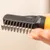 Close-up van een ontklittingskam met metalen tanden en een ergonomisch handvat, vastgehouden door een hand. Close-up van een ontklittingskam met metalen tanden en een ergonomisch handvat, vastgehouden door een hand.