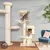 Multi-level cat tree with platforms, scratching posts, soft beds and two cats climbing and resting on it, shown in a living room setting.