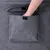 Hand greift in eine graue Stofftasche mit Klettverschluss, befestigt an einem Möbelstück.