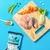 Ingredients including raw fish, chicken, carrot, fennel, peas, seeds, a capsule and a sachet of Pooch & Mutt Health & Digestion wet food displayed on a blue background.