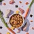 Bowl of cubed pet food surrounded by raw chicken pieces, carrots, carrot slices, rice grains, seaweed squares and yellow root vegetables, showing visible ingredients.