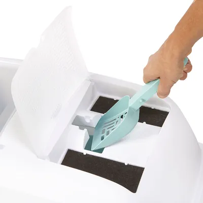 Pelle en plastique turquoise utilisée pour nettoyer une litière pour chat blanche avec couvercle ouvert et filtres visibles.