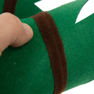 Gros plan sur une main tenant un objet en feutre vert avec bande marron, matière textile visible.