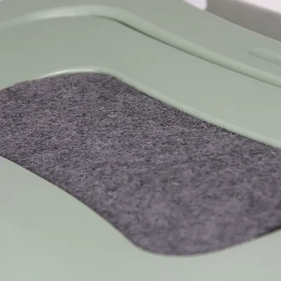 Gros-plan al unei suprafețe de fetru gri pe un cadru din plastic verde, posibil parte a unui produs sau accesoriu pentru animale.
