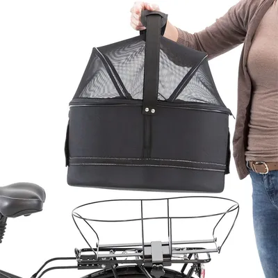Borsa trasportino nera con rete e manico, tenuta da una persona sopra un portapacchi di bicicletta. Materiale visibile: tessuto e rete.