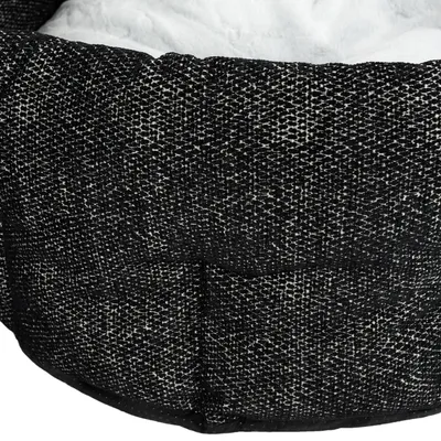 Dettaglio di una cuccia per animali con esterno in tessuto nero e bianco e interno imbottito bianco visibile.