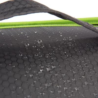 Gros plan sur tissu à motif hexagonal noir avec gouttes d’eau en surface et poignée grise, bordure verte visible. Le matériau semble imperméable.