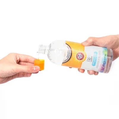 En hand häller vätska från en Arm & Hammer Fresh Spectrum-flaska i en gul mätkopp. Produkt för husdjursvård synlig.