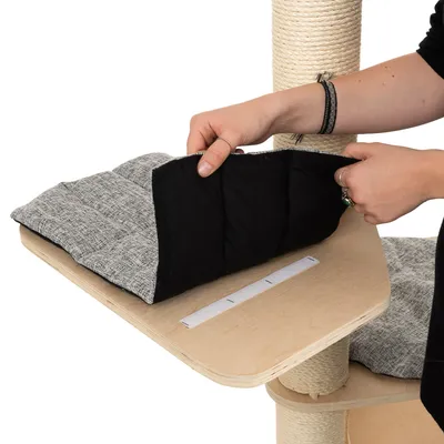 Käsi näyttää irrotettavaa, pehmustettua tyynyä tarrakiinnityksellä raapimispuun puualustalla.