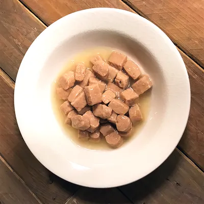 Valkoisella lautasella paloiteltua märkäruokaa hyytelössä tai kastikkeessa, ei näkyvää tuotemerkkiä tai pakkausta.