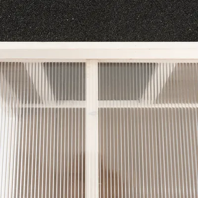 Toit en plastique transparent nervuré avec cadre en bois et revêtement supérieur noir visible, vue rapprochée du matériau et de la structure.