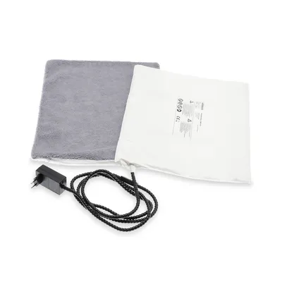 Elektrische Heizmatte mit grauem Bezug, Netzteil und Kabel. Weisse Bedienungsanleitung mit Sicherheitshinweisen sichtbar.