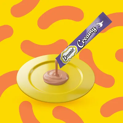 Saqueta Dreamies Creamy a verter creme castanho claro num prato amarelo. Texto visível: Dreamies Creamy com ilustração de pato branco na embalagem.