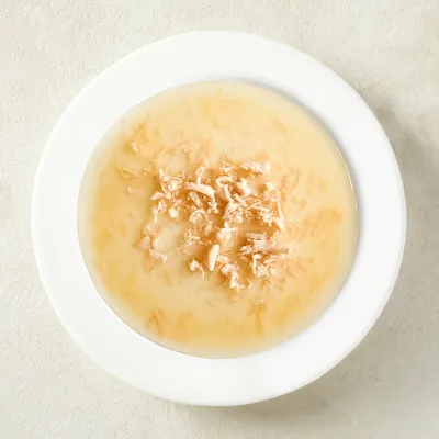 Nahaufnahme eines weißen Tellers mit feuchten, zerkleinerten Hühnerstücken in heller Brühe.