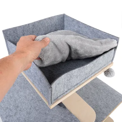 Hand legt graues, weiches Kissen in eine Filzbox auf einem mehrstöckigen Holzgestell mit Spielball.