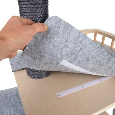 Hand showing grey felt pad with hook-and-loop fastener on wooden platform, suitable for attachment to scratching post.