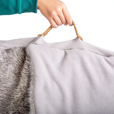Hand hält eine graue Tragetasche mit Kunstfell-Innenseite und geflochtenem Griff aus braunem Material.