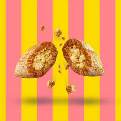 Croqueta de pienso partida por la mitad, mostrando relleno cremoso y trozos pequeños alrededor. Fondo con franjas verticales rosas y amarillas.