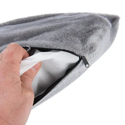 Hand öffnet grauen, weichen Bezug mit Reissverschluss, darunter sichtbare weisse Innenfüllung.