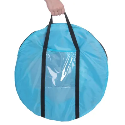 Rund blå väska i tyg med svarta handtag och genomskinlig plastficka framtill, hålls i handen. Ingen synlig text eller varumärke.