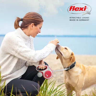 Flexi. Αυτόματες λουρίδες. Κατασκευάζεται στη Γερμανία. Γυναίκα κρατάει κόκκινη Flexi ρολό-λουρί, σκύλος κάθεται και ταΐζεται.