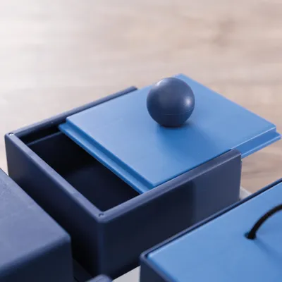 Giocattolo blu con coperchio scorrevole e manico a sfera, adatto per attività interattive.