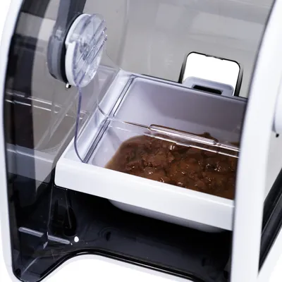 Nahaufnahme eines automatischen Futterspenders mit geöffneter Klappe und einer Schale mit Nassfutter.