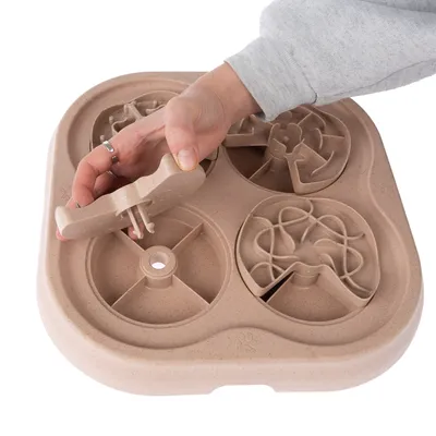 Hand demonstrating the use of a beige interactive feeding toy with four different puzzle elements.