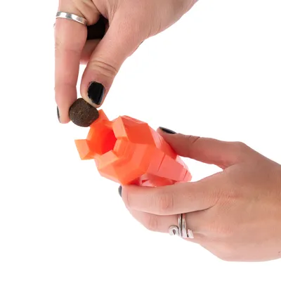Una mano riempie un gioco arancione con snack rotondi. Dimostrazione dell’uso di un distributore di cibo per pet.