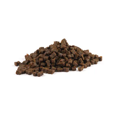Morceaux de friandises bruns en forme de petits cylindres, présentés en tas sur fond blanc. Aucun emballage ou marque visible.