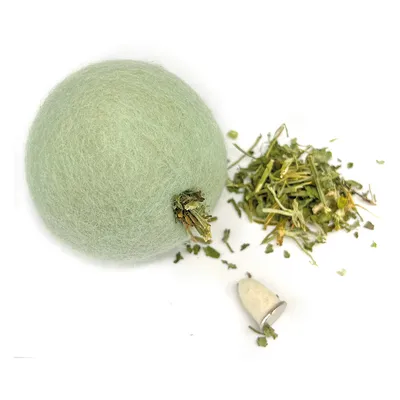 Balle en laine verte avec embout métallique, accompagnée d’un petit tas de feuilles et tiges séchées vertes sur fond blanc. Aucun texte ou marque visible.