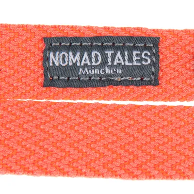 Nomad Tales München. Etikett på orangefärgat, vävt material.