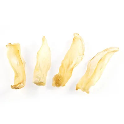 Čtyři kusy sušených žvýkacích pamlsků světlé barvy, bez obalu, na bílém pozadí.