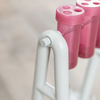Detail van wit kunststof frame met roze transparante draaibare bekers, elk met drie openingen in het deksel. Materiaal: kunststof.