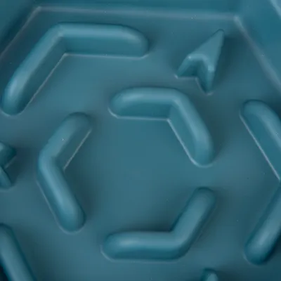 Gros plan sur un fond en plastique bleu avec des reliefs en forme de flèches et de chevrons, typique d’une gamelle anti-glouton pour animaux.
