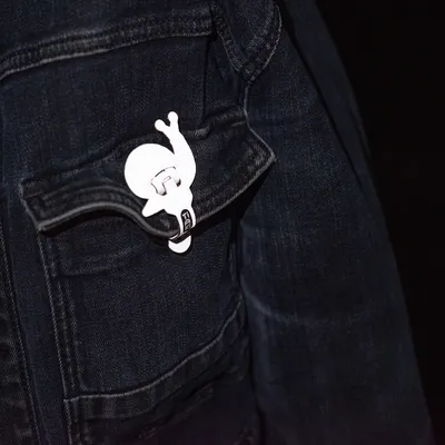 Clip blanco en forma de caracol, sujeto al bolsillo de una chaqueta vaquera oscura.
