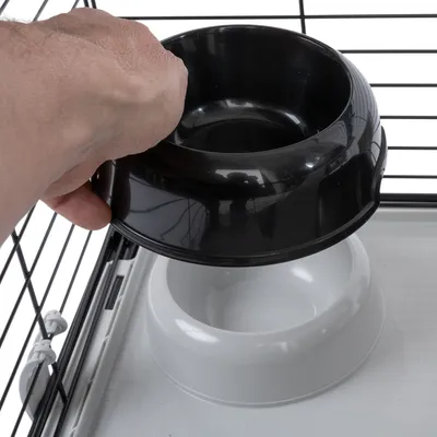 Hand platziert schwarzen Futternapf in weissen Halter innerhalb eines Käfigs. Zeigt einfache Handhabung des Napfsystems.